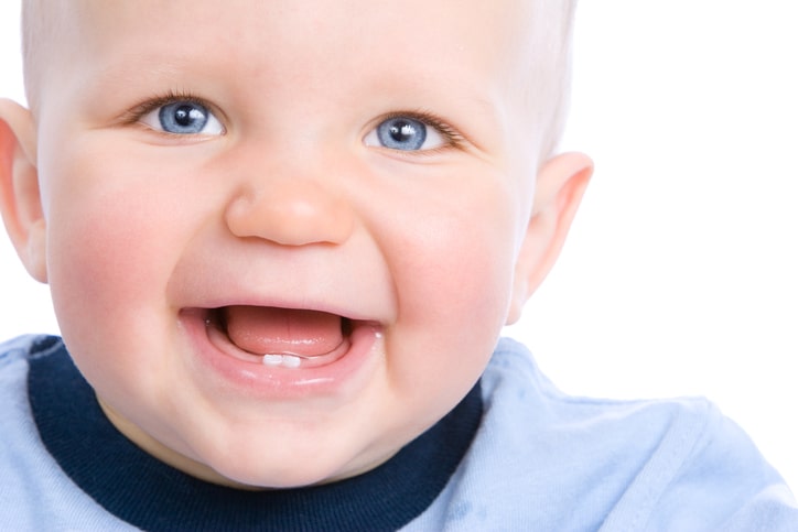 Cute baby looking into camera and laughing, showing two teeth